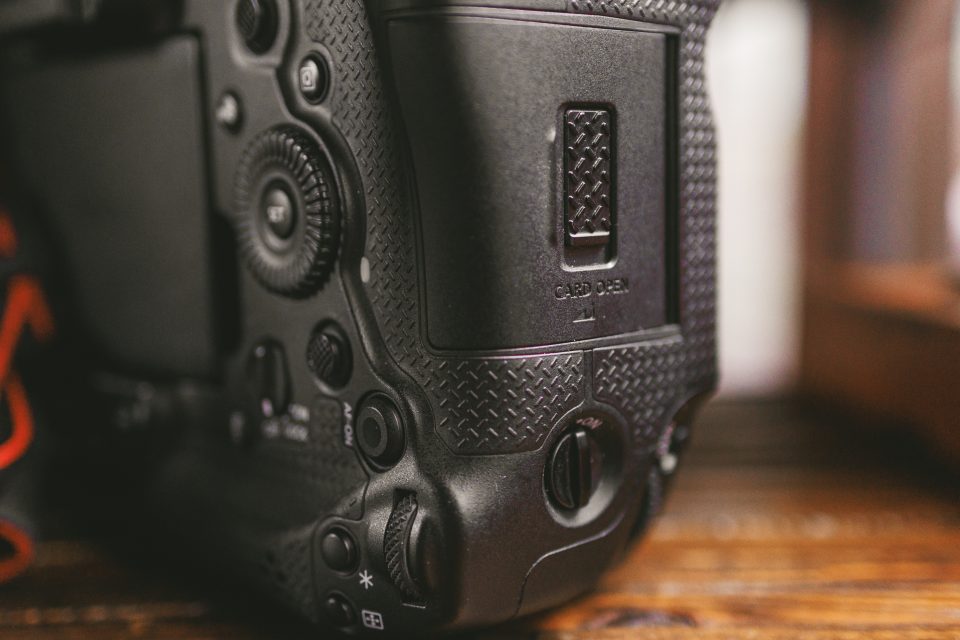 Close-up of the side of a black digital camera showing textured grip, buttons, and memory card compartment labeled "CARD OPEN.